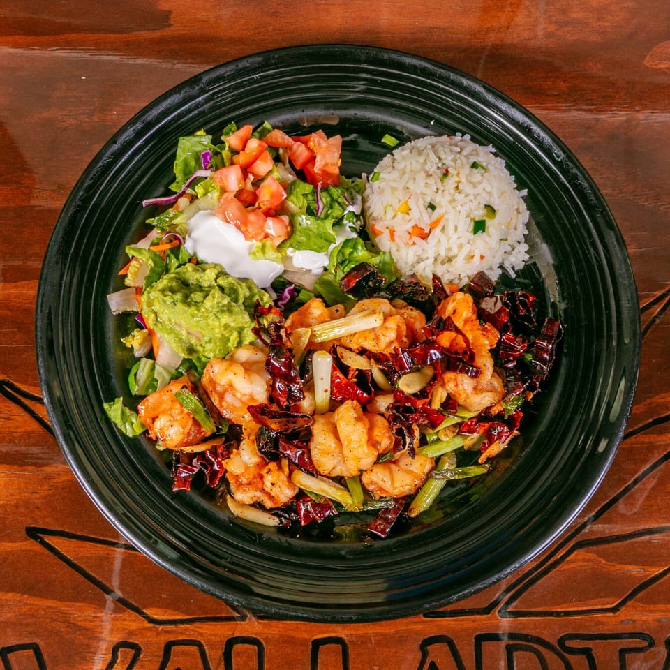Vallarta Tequila Bar's spicy shrimp dish with rice, guacamole, sour cream, and salad on a black plate.