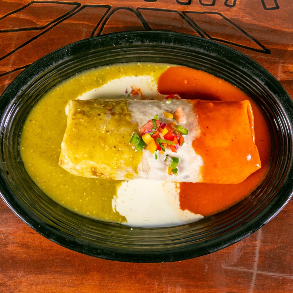 A Vallarta Tequila Bar burrito covered in green and red sauces, topped with pico de gallo.