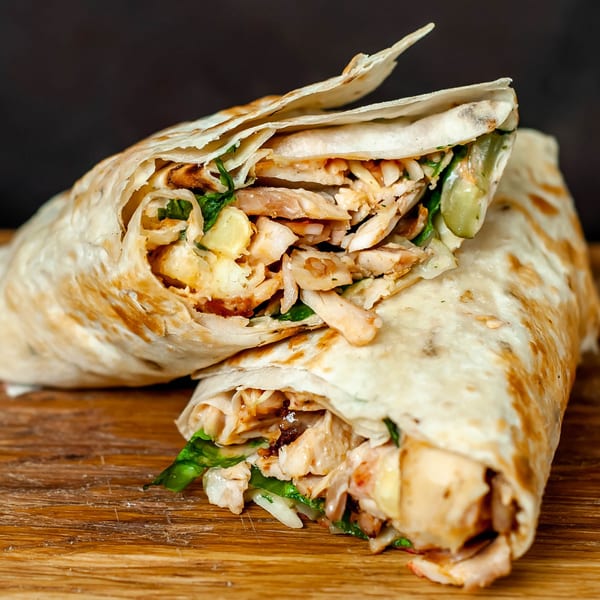 Two chicken shawarmas with lettuce and sauce, wrapped in flatbread, on a wooden board.