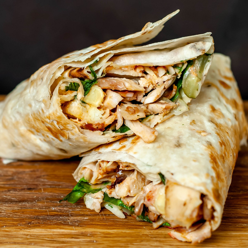 Two chicken shawarmas with lettuce and sauce, wrapped in flatbread, on a wooden board.