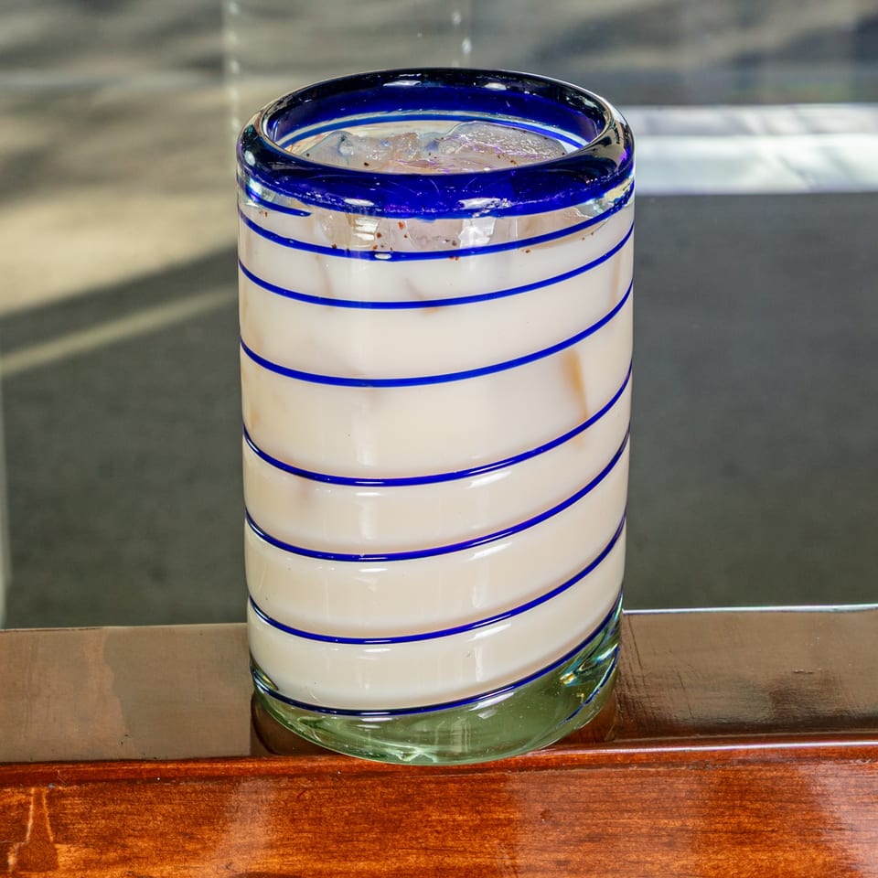 A Mexican horchata drink in a blue and white striped glass on a wooden surface.