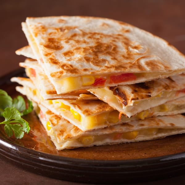 Stack of golden-brown quesadilla wedges filled with melted cheese, corn, and red peppers, garnished with cilantro.