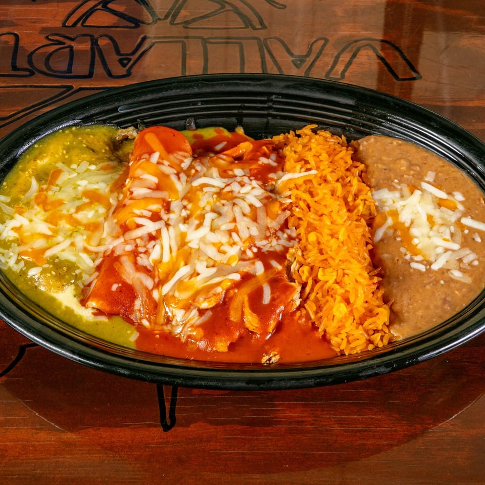Mexican enchiladas with green and red sauce, rice, and refried beans, topped with cheese.