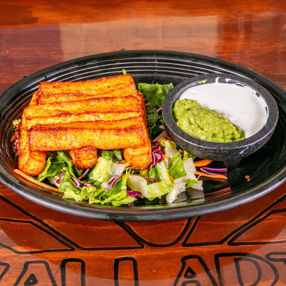 Fried cheese sticks on a bed of lettuce with guacamole and sour cream in a black bowl.