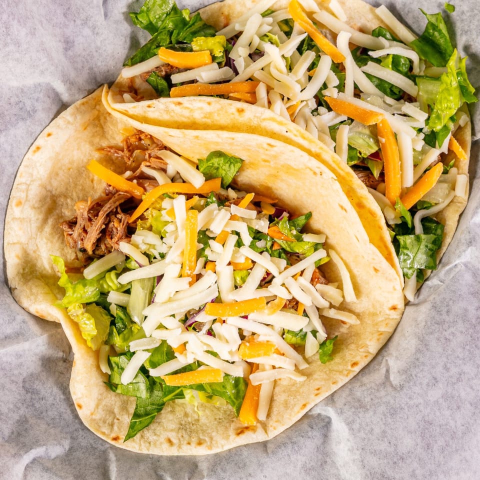 Two Vallarta Tequila Bar tacos with shredded meat, lettuce, and cheese on white paper.